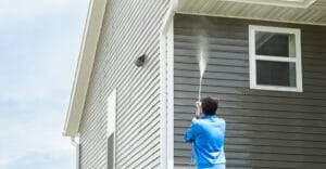 man pressure washing home wall